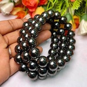 Puede incluir: Un brazalete de cuentas de hematites negras con múltiples hileras de cuentas redondas. El brazalete está hecho de piedras de hematites naturales.