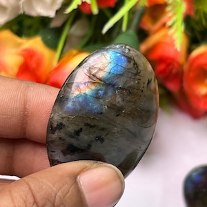 May include: A smooth, oval-shaped labradorite gemstone with iridescent blue, green, and gold colors. The stone is polished and has a natural, organic shape.