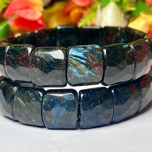 May include: Two stacked bracelets made of dark blue and black gemstone beads with a shimmery, iridescent finish.