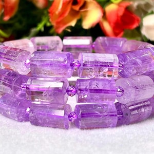 May include: A purple amethyst bracelet made of faceted, rectangular beads. The beads are translucent and have a light purple hue.