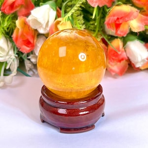 May include: A bright yellow crystal ball on a dark red wooden stand. The ball is smooth and shiny, with a slight sparkle.
