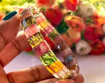 May include: A multi-colored gemstone bracelet with square-shaped beads in shades of pink, green, yellow, and blue. The bracelet is made of natural gemstones and is a beautiful and unique piece of jewelry.