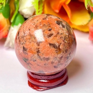 May include: A red and white crystal sphere on a wooden stand. The sphere is polished and has a natural, marbled appearance.