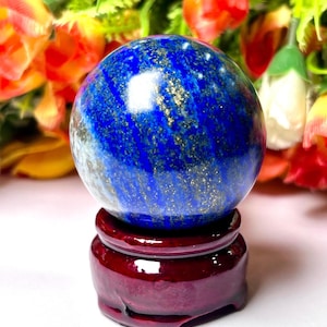 May include: A blue and gold lapis lazuli sphere on a dark red wooden stand. The sphere is polished and has a smooth surface.