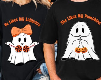 May include: Black t-shirts with Halloween-themed graphics. One shirt features a ghost with a bow holding lollipops, the text reads "He Likes My Lollipops." The other shirt shows a ghost with pumpkins, text reads "She Likes My Pumpkins."