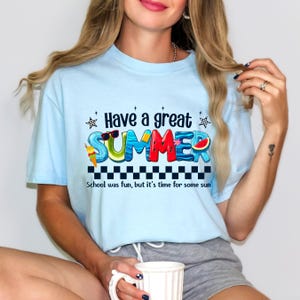 May include: A light blue t-shirt with a graphic print of the word "SUMMER" in colorful letters with summer-themed illustrations. The text "Have a great summer" is above the word "SUMMER" and the text "School was fun, but it's time for some sun" is below the word "SUMMER".