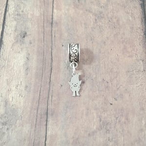 May include: Silver charm featuring a small cartoon elf with a pointed hat and a smiling face. The charm is attached to a silver bead with an ornate design.
