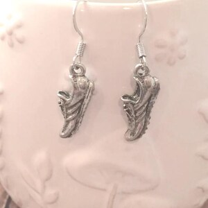 May include: A pair of silver earrings featuring a shoe design. The earrings are hanging from a white surface.