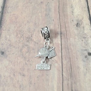 May include: Silver charm with a ball of yarn, crochet hook, and a small sign that reads "I love 2 crochet".