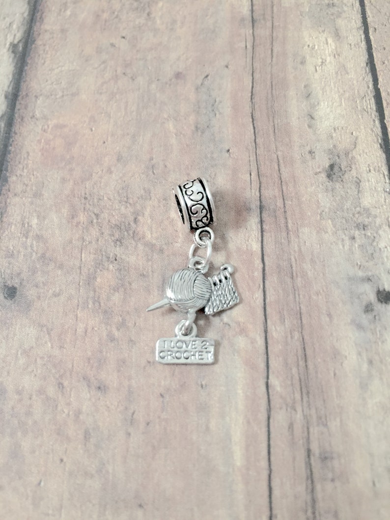 May include: Silver charm with a ball of yarn, crochet hook, and a small sign that reads "I love 2 crochet".