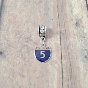 May include: Silver charm with a blue and red interstate highway sign with the number 5 on it.