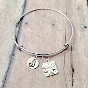 May include: A silver expandable bangle bracelet with a charm of a starburst design and a charm with the letter "S" engraved on it.