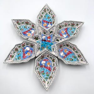 May include: A star-shaped ceramic serving set consisting of a central five-pointed star bowl surrounded by five leaf-shaped bowls. Each piece features hand-painted illustrations of two figures in traditional headwear against a blue background.