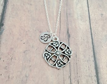 May include: A silver necklace with a Celtic knot pendant and a small charm with the letter "B" on it.