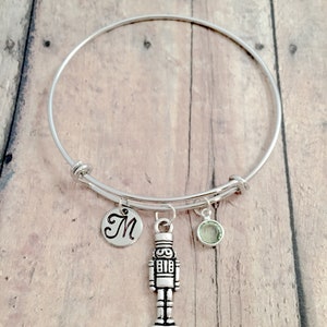May include: A silver charm bracelet with a nutcracker charm, a green crystal charm, and a silver charm with the letter M.