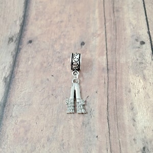 May include: Silver charm with a detailed design of a pair of pants with ruffles. The charm is attached to a silver ring with a decorative design.