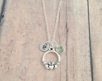 May include: A silver necklace with a Celtic knot pendant, a small green gemstone, and a silver charm with the letter "R" engraved on it.