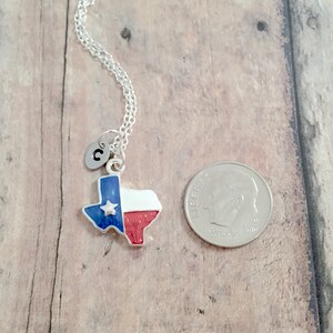 May include: A silver necklace with a charm of the state of Texas with the Texas flag colors, red, white, and blue. The charm also has a small silver star. The necklace has a silver initial charm with the letter "C" on it. The necklace is shown next to a US dime for size comparison.