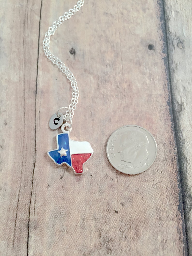 May include: A silver necklace with a charm of the state of Texas with the Texas flag colors, red, white, and blue. The charm also has a small silver star. The necklace has a silver initial charm with the letter "C" on it. The necklace is shown next to a US dime for size comparison.