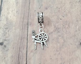 May include: Silver spinning wheel charm with a decorative scroll design. The charm is attached to a silver bead with a decorative scroll design.
