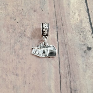 May include: Silver charm in the shape of a small house with a detailed design. The charm is attached to a silver bead with a decorative design.