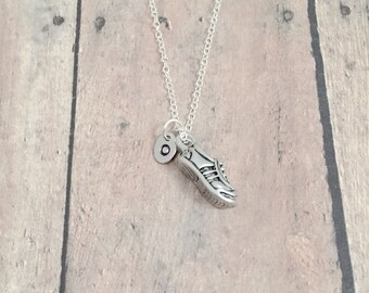 May include: A silver necklace with a small silver shoe charm and a silver initial charm. The necklace is on a wooden background.