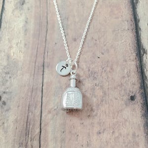 May include: Silver necklace with a charm of a tequila bottle and a small charm with the letter T.