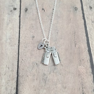 May include: A silver necklace with a charm of a pair of jeans and a small round charm with the letter "T" on it.