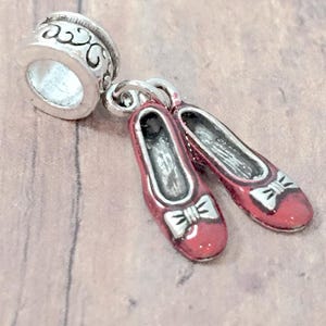 May include: A silver charm with a pair of red ruby slippers, a popular symbol from the Wizard of Oz.