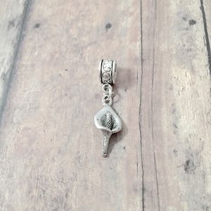 May include: Silver charm featuring a stylized calla lily flower. The charm is attached to a silver chain and a silver bead with an ornate design.