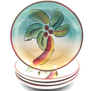 May include: A stack of ceramic plates with a hand-painted tropical palm tree design. The plates feature a turquoise sky, tan sand, and a red, yellow, and green palm tree. The rims are red, and the plates are stacked on a metal stand.