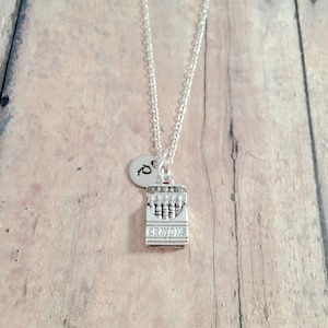 May include: A silver necklace with a charm that looks like a box of crayons. The charm has the word "Crayons" on it. The necklace also has a small silver disc with the letter "P" on it.