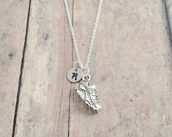 May include: Silver necklace with a running shoe charm and a small initial charm. The initial charm is a silver circle with the letter "N" engraved on it.