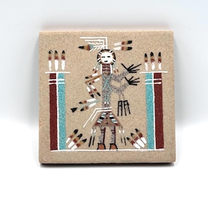May include: Square, tan-colored tile with a Native American sand painting design. The artwork features a central figure with a white face, surrounded by geometric patterns in red, blue, black, and white. The tile is approximately 4 inches square.