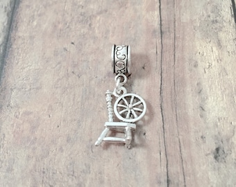 May include: Silver charm featuring a spinning wheel with a detailed design. The charm is attached to a silver bead with a decorative pattern.