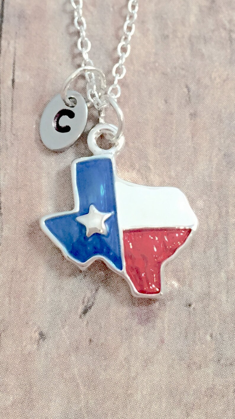 May include: A silver necklace with a charm shaped like the state of Texas. The charm is painted with the Texas flag colors: blue, white, and red. A silver charm with the letter "C" is attached to the necklace.