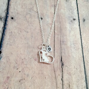 May include: Silver necklace with a heart-shaped pendant featuring a chihuahua silhouette and a small charm with the letter "D".