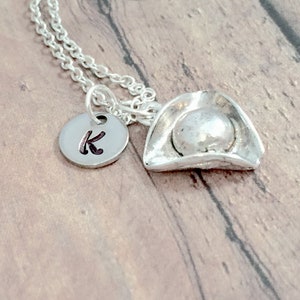 May include: A silver necklace with a silver pirate hat charm and a silver disc charm with the letter K engraved on it.