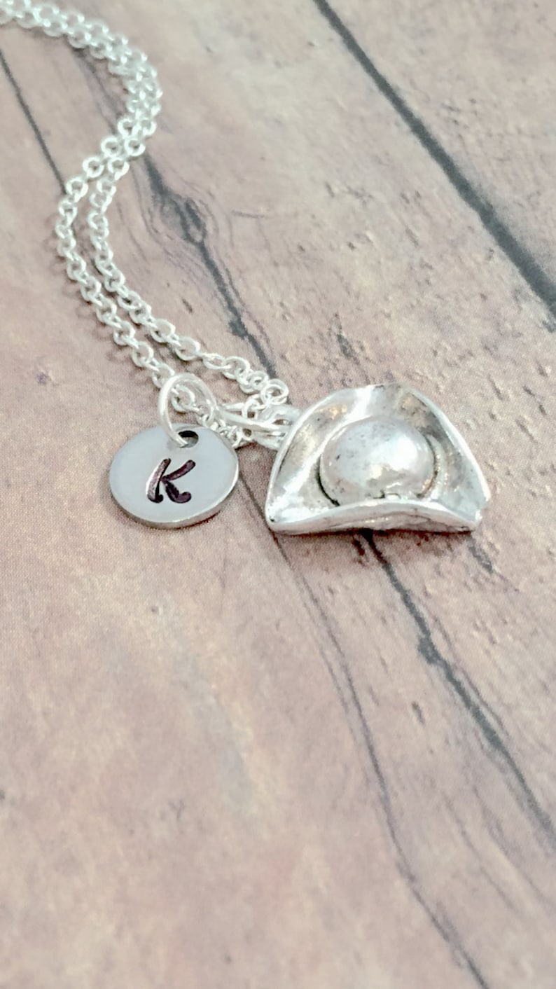 May include: A silver necklace with a silver pirate hat charm and a silver disc charm with the letter K engraved on it.