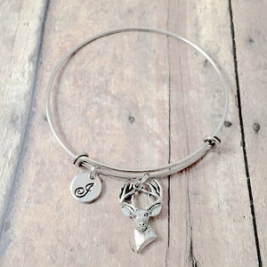 May include: A silver expandable bangle bracelet with a silver charm of a deer head and a silver charm with the letter "J" on it.