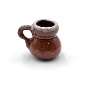 May include: A small, brown ceramic mug with a handle. The mug has a rounded base and a slightly flared rim with a lighter-colored band. The handle is curved and attached to the side of the mug. The mug is likely used for drinking.