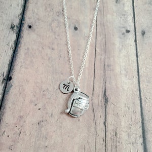 May include: Silver necklace with a honey pot charm and an initial 'M' charm. The necklace is on a wooden background.