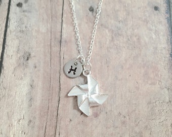 May include: A silver necklace with a small silver charm in the shape of a pinwheel and a silver disc charm with the letter "H" on it.