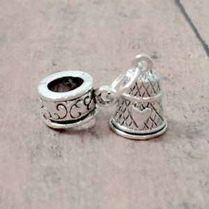 May include: Silver charm with a bell design and a small heart on the front. The bell is attached to a silver spacer bead with an ornate design.