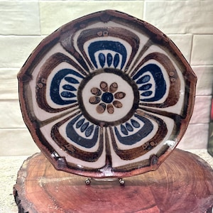 May include: A white ceramic mug with a black handle and the text "But First, Coffee" in a bold, black font. The mug is set against a blurred background, suggesting a cozy setting.