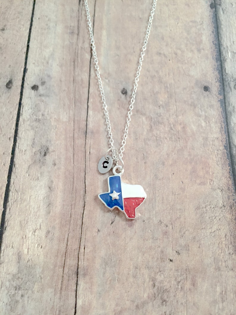 May include: Silver necklace with a charm shaped like the state of Texas, featuring the Texas flag colors of blue, white, and red. The charm also has a small silver star. The necklace has a silver initial charm with the letter "C" on it.