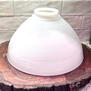 May include: A white, dome-shaped glass lampshade with a textured surface. The lampshade has a rounded top and a slightly flared base. It is sitting on a wooden surface.