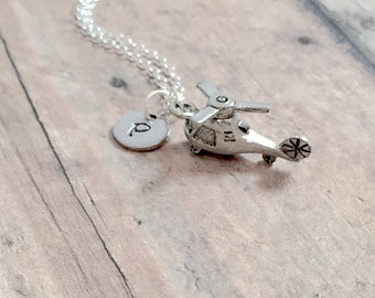 May include: Silver necklace with a small helicopter charm and a letter 'P' charm. The necklace is on a wooden surface.