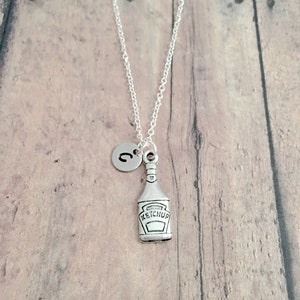 May include: Silver necklace with a ketchup bottle charm and a letter 'C' charm.