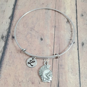 May include: A silver bangle bracelet with a charm of a Roman warrior's helmet and a small charm with the letter "L" on it.